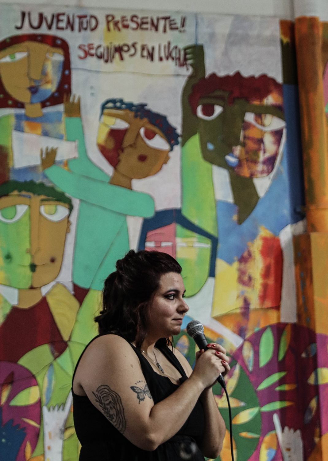 Victoria hablando frente a un mural que dice «Juventud presente, seguimos en lucha»